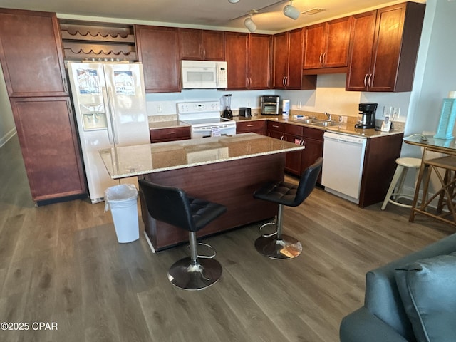 kitchen featuring wood finished floors, white appliances, a sink, and a breakfast bar area