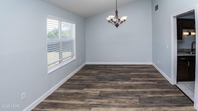 unfurnished dining area featuring a sink, vaulted ceiling, baseboards, a chandelier, and wood finished floors