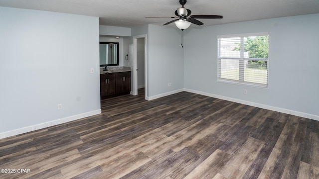 unfurnished living room featuring ceiling fan, baseboards, dark wood-style flooring, and a sink