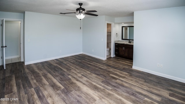 unfurnished living room featuring baseboards, a sink, ceiling fan, and dark wood-style flooring