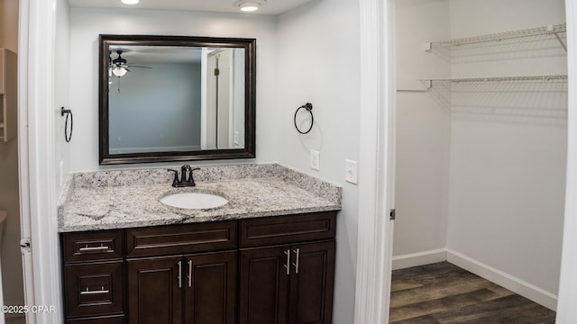 bathroom featuring baseboards, a spacious closet, wood finished floors, ceiling fan, and vanity