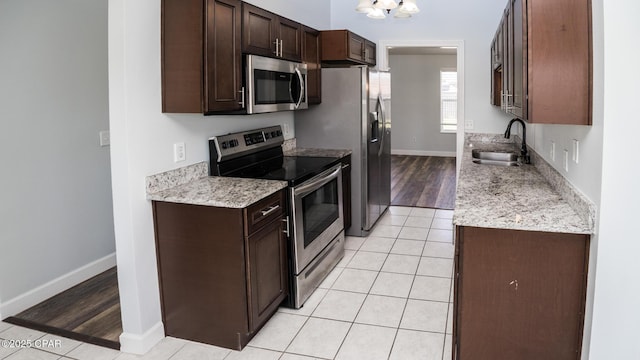 kitchen with light tile patterned floors, dark brown cabinetry, stainless steel appliances, and a sink