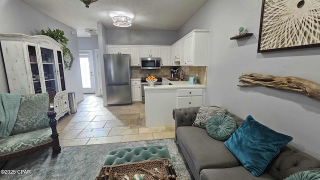 kitchen with white cabinets, stainless steel appliances, light countertops, a sink, and tasteful backsplash