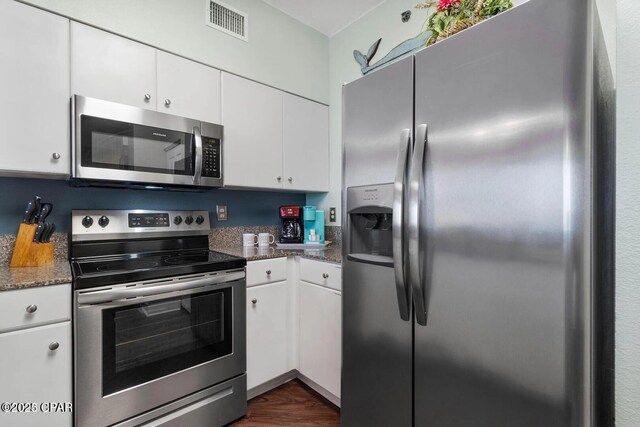 9900 S Thomas Dr Unit 819, Panama City Beach, FL 32408 - kitchen featuring appliances with stainless steel finishes, dark stone counters, white cabinetry, dark wood-type flooring, and visible vents