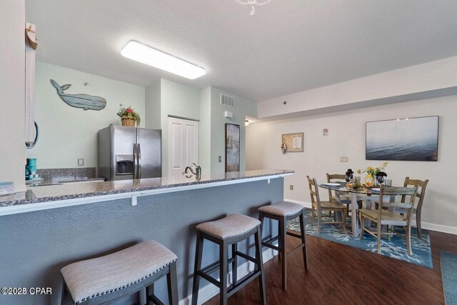 9900 S Thomas Dr Unit 819, Panama City Beach, FL 32408 - kitchen with dark wood-style flooring, stainless steel fridge, stone countertops, baseboards, and visible vents