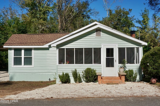 view of front facade featuring entry steps, a sunroom, and roof with shingles