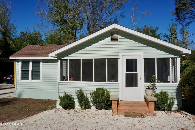 rear view of house featuring entry steps, a shingled roof, and a sunroom