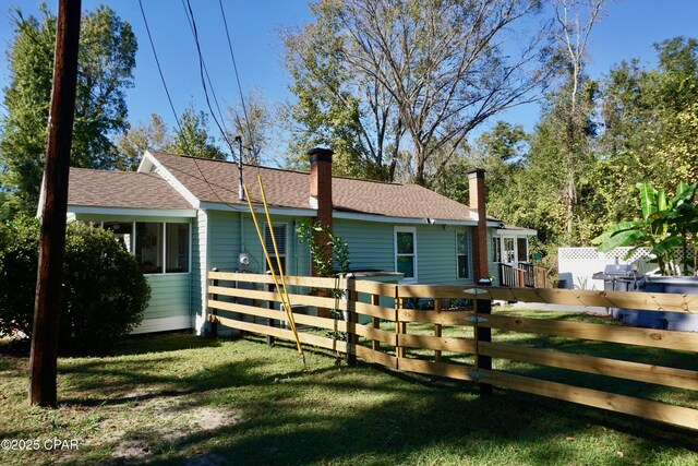 view of side of property with fence, a chimney, and a yard