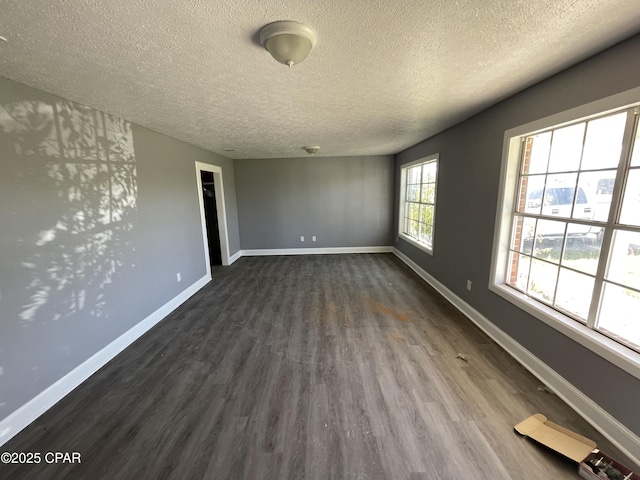 empty room featuring a textured ceiling, dark wood-type flooring, and baseboards