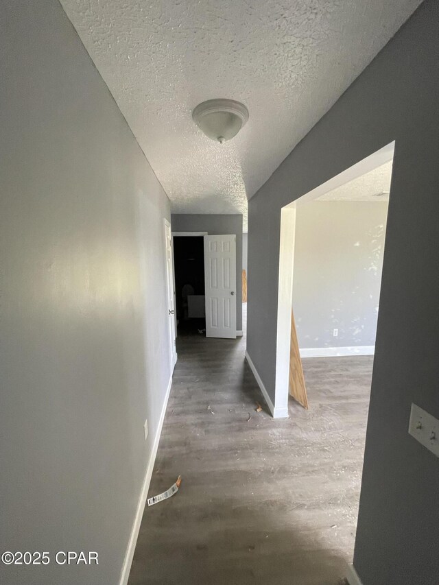 hall with a textured ceiling, wood finished floors, and baseboards