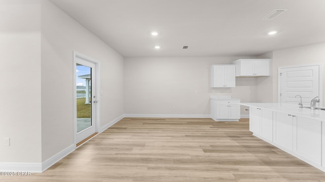 unfurnished dining area featuring recessed lighting, baseboards, a sink, and light wood-style flooring