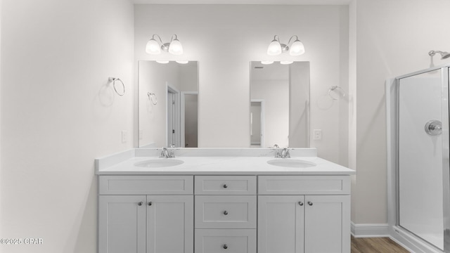 bathroom with double vanity, a sink, wood finished floors, and a shower stall