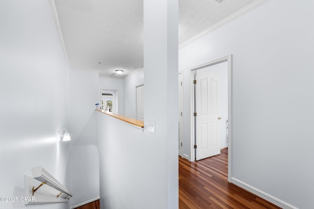 hallway featuring baseboards, a textured ceiling, ornamental molding, and wood finished floors