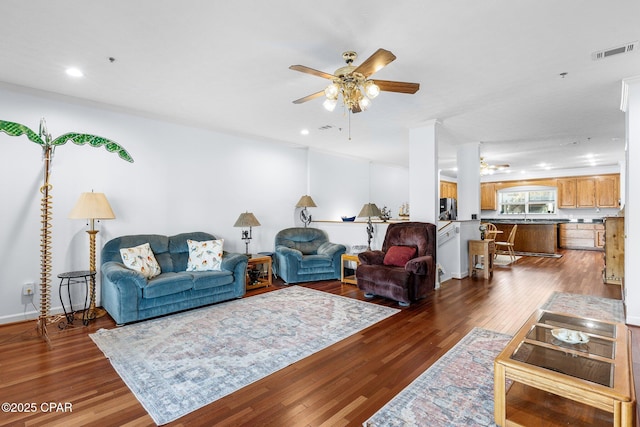 living area with visible vents, a ceiling fan, and dark wood finished floors