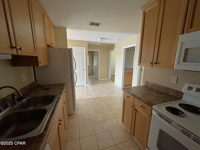 kitchen with dark countertops, a sink, white appliances, light tile patterned floors, and visible vents