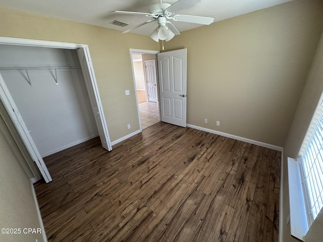 unfurnished bedroom featuring wood finished floors, visible vents, a closet, baseboards, and ceiling fan