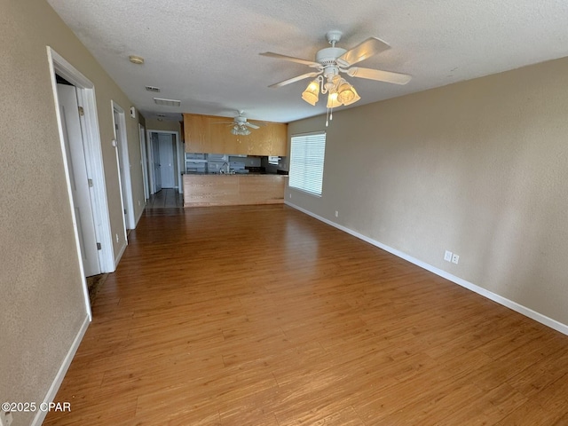 unfurnished living room with a ceiling fan, a textured ceiling, light wood-style floors, baseboards, and visible vents
