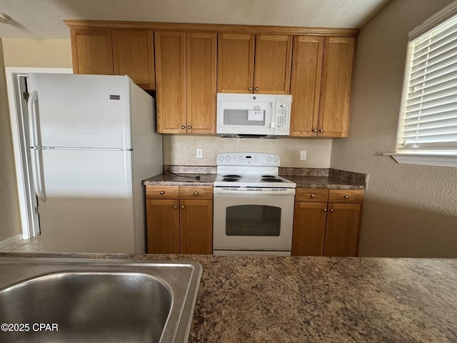 kitchen featuring brown cabinets, a textured wall, a sink, and white appliances
