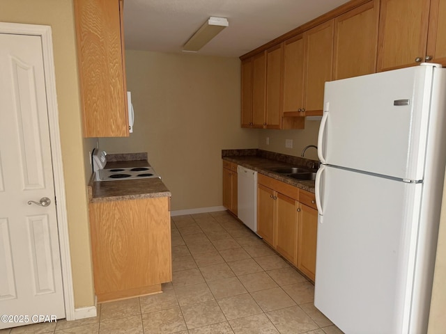 kitchen featuring dark countertops, a sink, light tile patterned flooring, white appliances, and baseboards