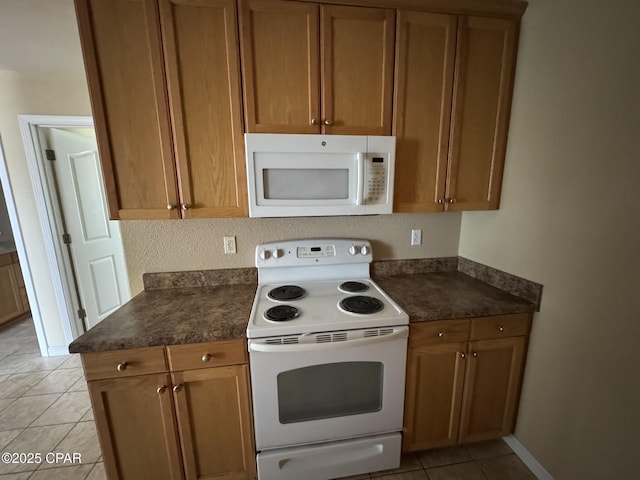 kitchen featuring dark countertops, baseboards, white appliances, brown cabinetry, and light tile patterned floors