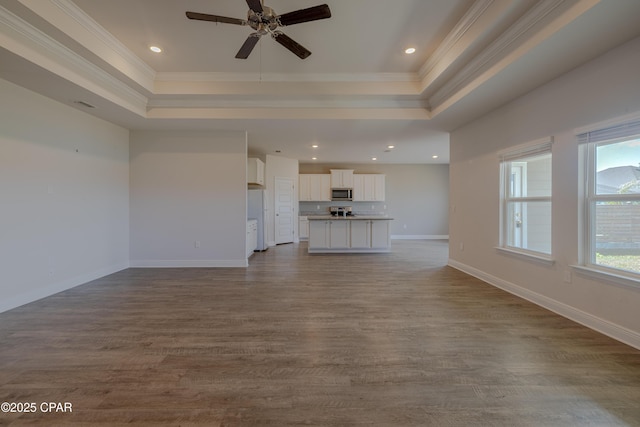 unfurnished living room with a raised ceiling, a ceiling fan, and crown molding