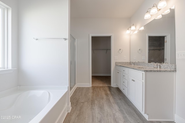 bathroom with a sink, double vanity, a walk in closet, a garden tub, and wood finished floors