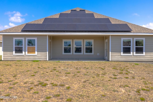 rear view of house with a yard, a shingled roof, and solar panels