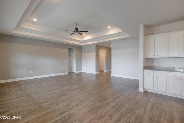 unfurnished living room featuring ornamental molding, ceiling fan, a tray ceiling, and baseboards