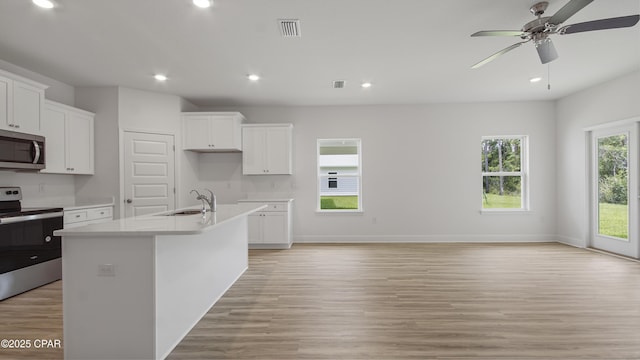 kitchen with a sink, an island with sink, light wood-style floors, ceiling fan, and appliances with stainless steel finishes