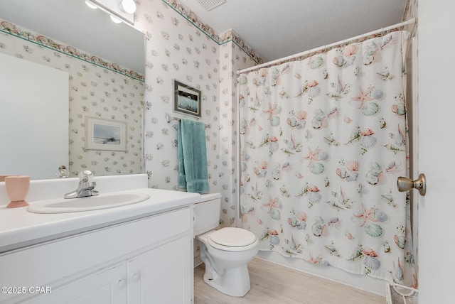 full bathroom with wallpapered walls, wood finished floors, toilet, vanity, and a textured ceiling
