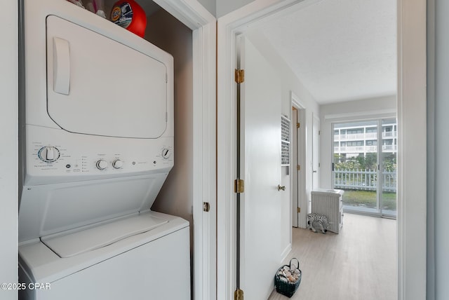washroom featuring stacked washer and dryer, wood finished floors, and laundry area