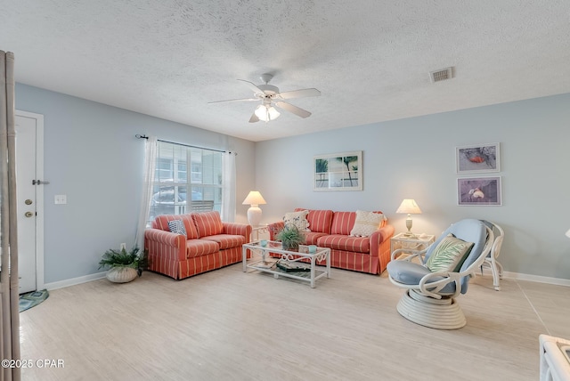 living area featuring wood finished floors, visible vents, a ceiling fan, baseboards, and a textured ceiling