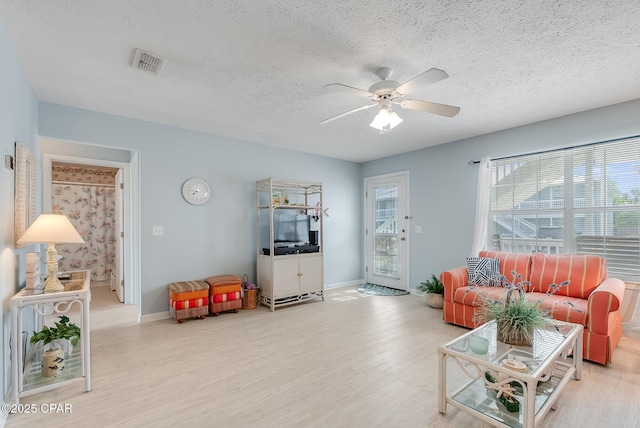 living area featuring wood finished floors, a textured ceiling, ceiling fan, baseboards, and visible vents