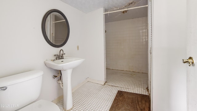 bathroom with tile patterned floors, a sink, a tile shower, toilet, and baseboards