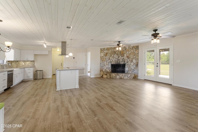 unfurnished living room featuring visible vents, ceiling fan, a stone fireplace, and light wood finished floors