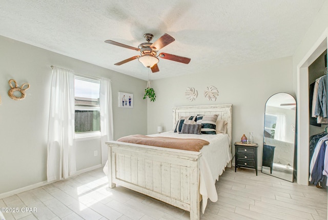 bedroom featuring baseboards, ceiling fan, light wood finished floors, and a textured ceiling