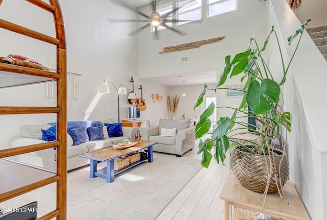 living area with ceiling fan, visible vents, wood finished floors, a high ceiling, and stairs