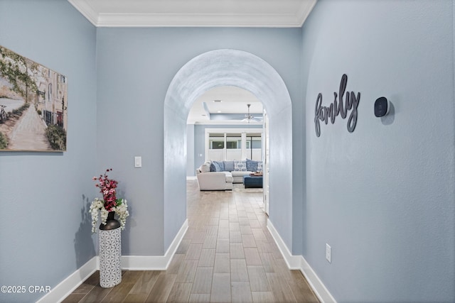 hall with crown molding, arched walkways, baseboards, and wood finished floors