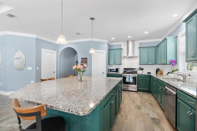 kitchen featuring green cabinetry, a kitchen island, stainless steel appliances, and wall chimney exhaust hood