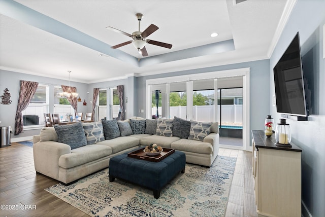 living area with crown molding, a tray ceiling, wood finished floors, and ceiling fan with notable chandelier