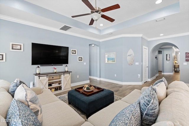 living room featuring arched walkways, a ceiling fan, baseboards, a tray ceiling, and visible vents