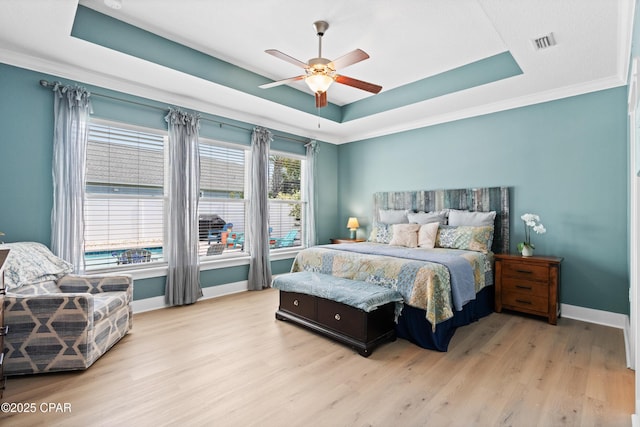 bedroom featuring light wood-style flooring, baseboards, a tray ceiling, visible vents, and ornamental molding
