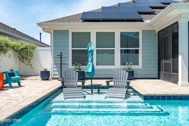 rear view of property featuring a shingled roof, solar panels, a patio area, and an outdoor pool