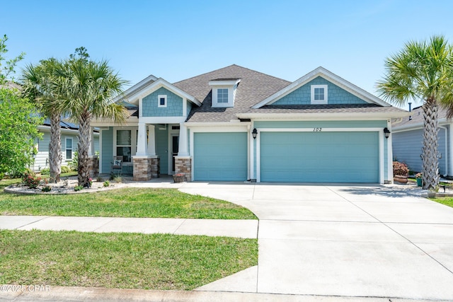 craftsman-style home featuring covered porch, a front lawn, concrete driveway, an attached garage, and a shingled roof