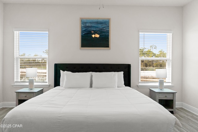 bedroom featuring baseboards, wood finished floors, and multiple windows