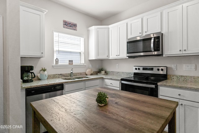kitchen featuring stainless steel appliances, light stone countertops, white cabinetry, and a sink