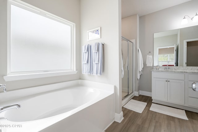 full bath featuring wood finished floors, a stall shower, a bath, vanity, and baseboards