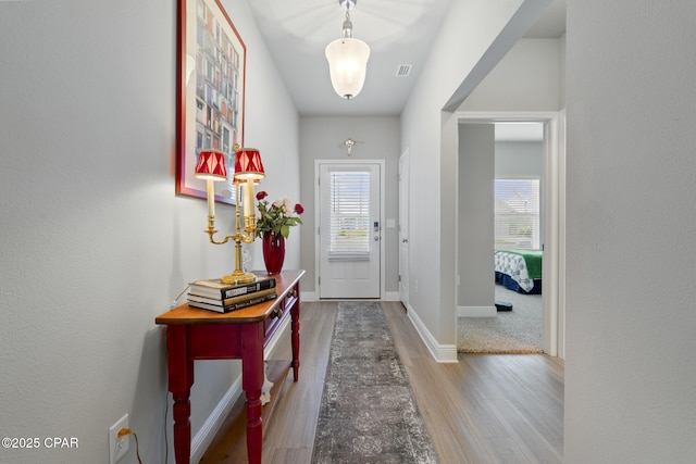 foyer entrance featuring baseboards, wood finished floors, and visible vents