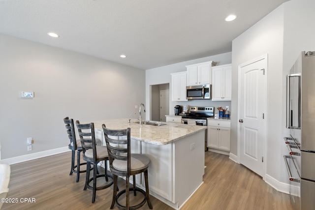 kitchen featuring a sink, an island with sink, light wood-type flooring, a breakfast bar area, and appliances with stainless steel finishes