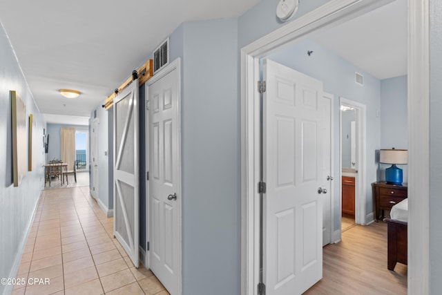 corridor with a barn door, visible vents, baseboards, and light tile patterned flooring